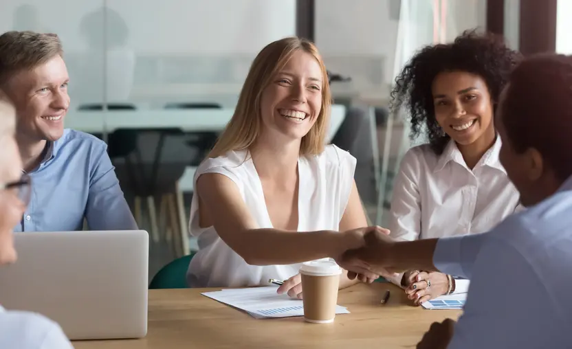 A diverse group of workers sit around the table and shake hands. Learn about how to surpass the grantmaking racial funding gap in this guide.