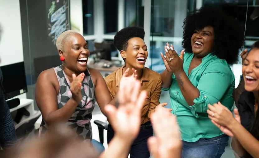 Group of African American women in circle clapping in business setting