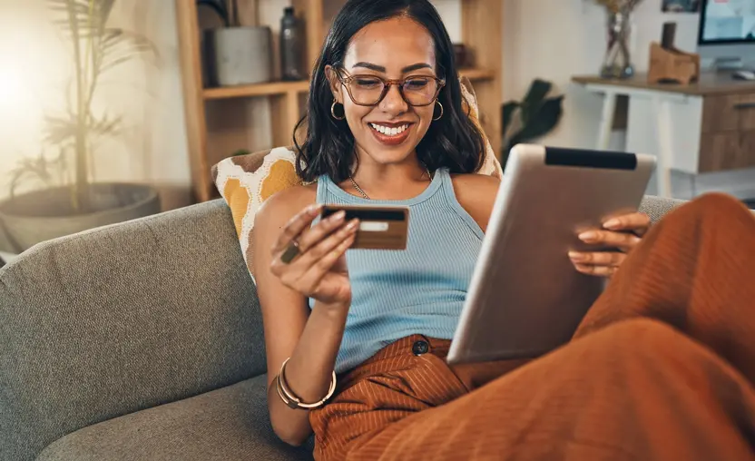 woman sitting on couch with ipad and credit card in hand