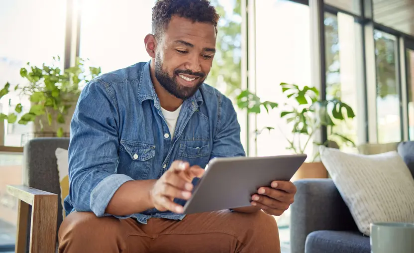 A man is sitting on his couch and using his tablet to review Bonterra Grants Management.