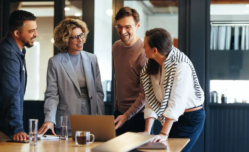 A team wraps up a meeting standing in front of a laptop