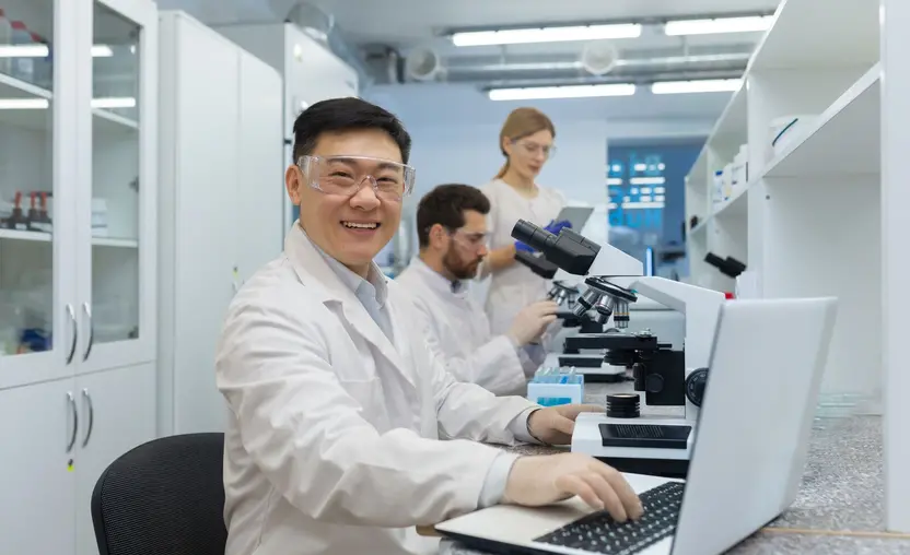 Man with microscope in white coat and goggles smiling and looking at camera