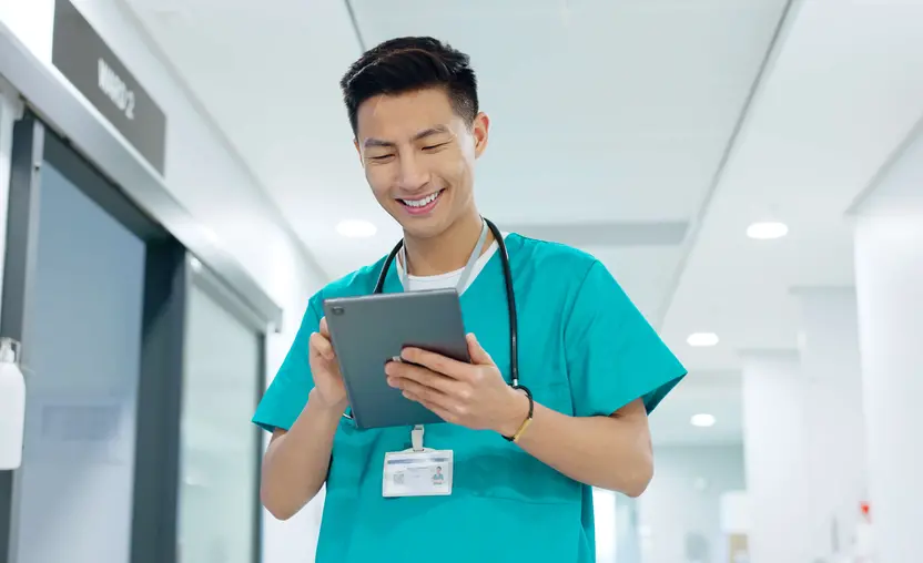 A doctor smiles while walking down a hall and reviewing data on a tablet.