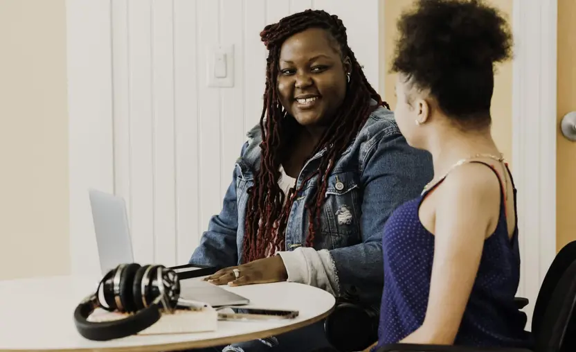 Two female coworkers meet at a coffee table with a laptop.