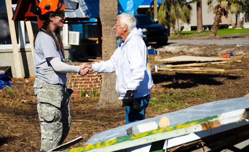 A relief worker shakes hands with a homeowner after a disaster.