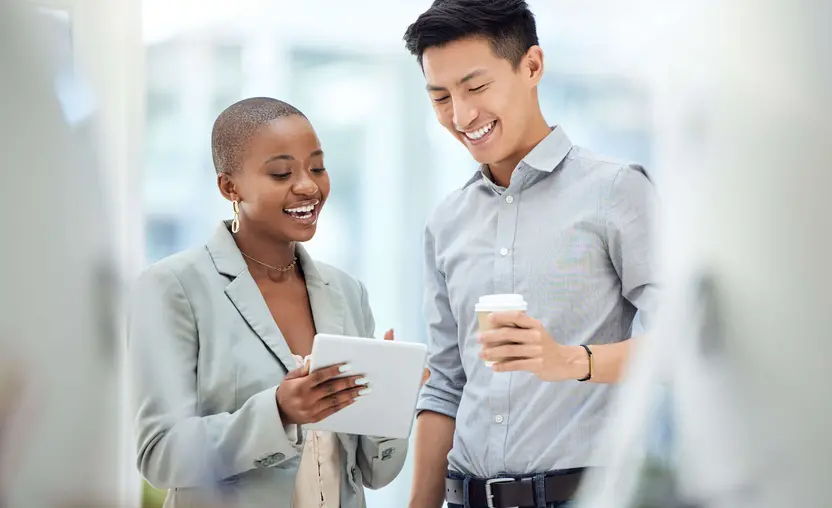 Two young coworkers smile while reviewing information on a tablet.