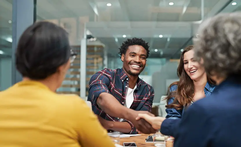 Team members happily shake hands during a meeting.