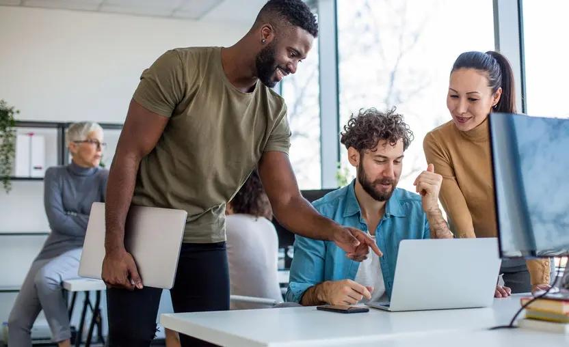 Three coworkers gathered around a laptop.