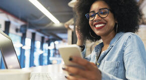 A smiling woman looks at her phone and reads an email created using our GivingTuesday email template.