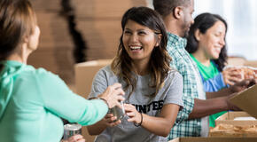 This image of a smiling woman loading cans into boxes represents the importance and impact of employee volunteer programs.