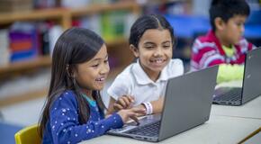 two little girls in school sitting in front of laptop computer