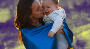 A mother wrapped in a Ukrainian flag kissing her baby.