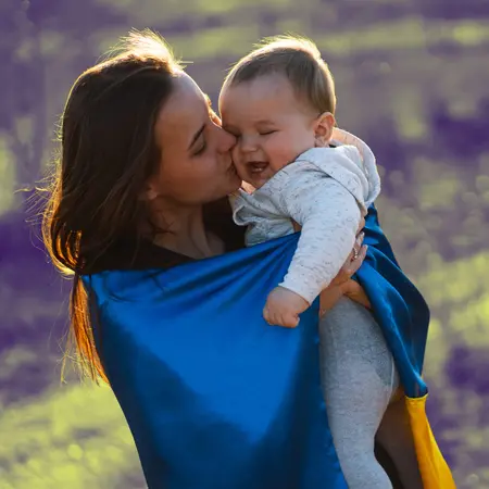 A mother wrapped in a Ukrainian flag kissing her baby.