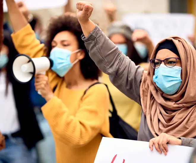 Muslim woman wearing protective face mask and supporting anti-racism movement with group of people on city streets.