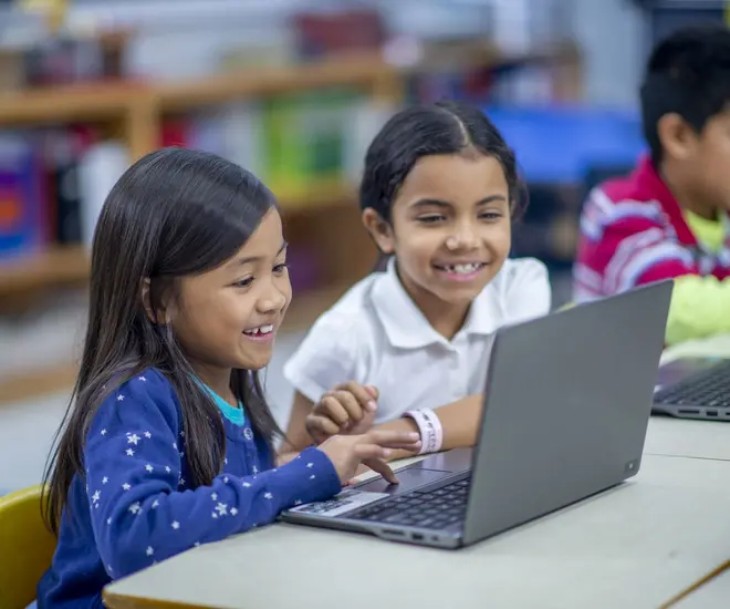 two little girls in school sitting in front of laptop computer