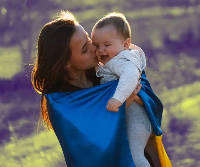 A mother wrapped in a Ukrainian flag kissing her baby.