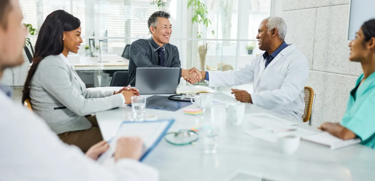 doctor shaking hands with business man at board table