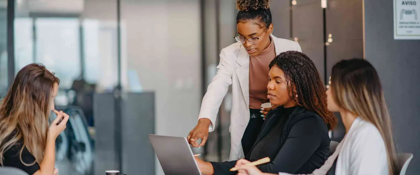 A group of women in an office look at a laptop and discuss their nonprofit CRM.