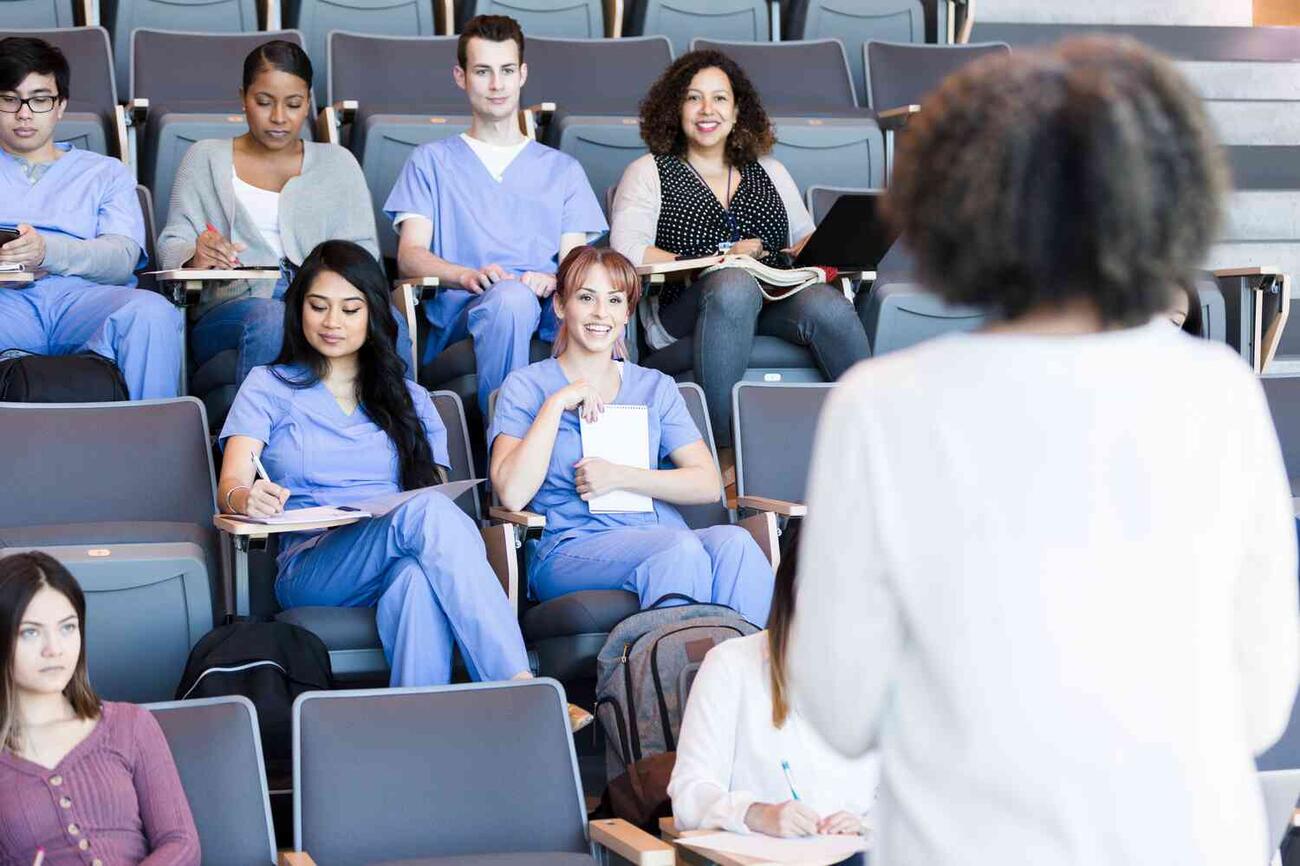 A group of medical students listen to a professorâ€™s lecture in an auditorium.