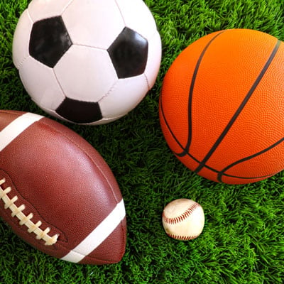 This photo of a football, soccer ball, basketball, and baseball represents the skills clinic fundraising event idea for sports teams.