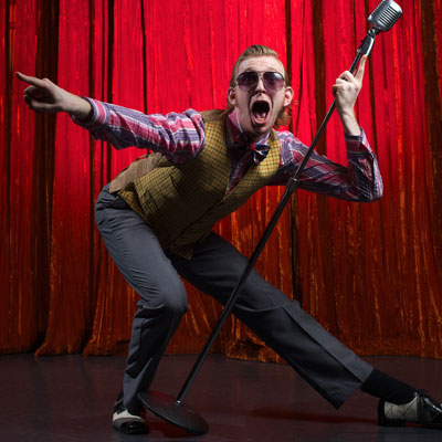 This photo of a young person performing on stage with a microphone demonstrates the appeal of a student variety show as a university fundraising event idea.