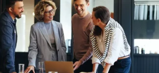 Four coworkers look at a laptop as they discuss their corporate matching gifts program