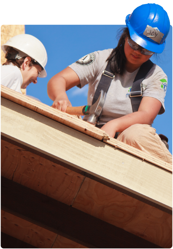 Two construction workers wearing hard hats build a house