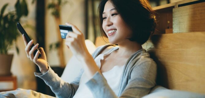 A smiling woman holds a credit card and her phone, representing text to donate