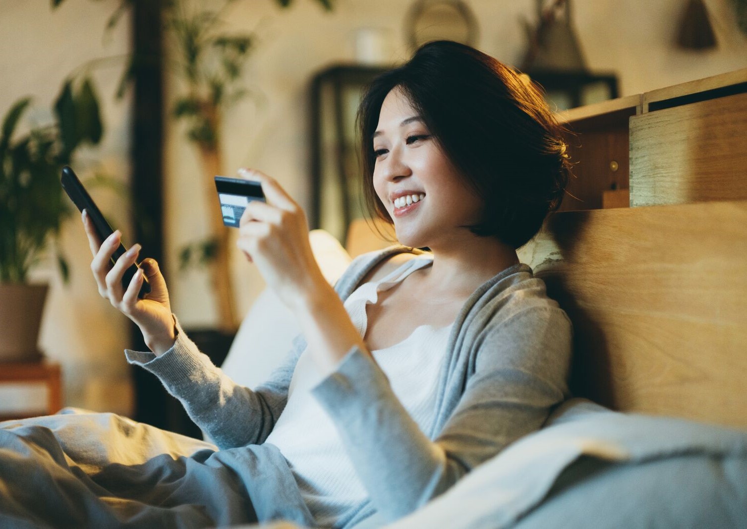 A smiling woman holds a credit card and her phone, representing text to donate