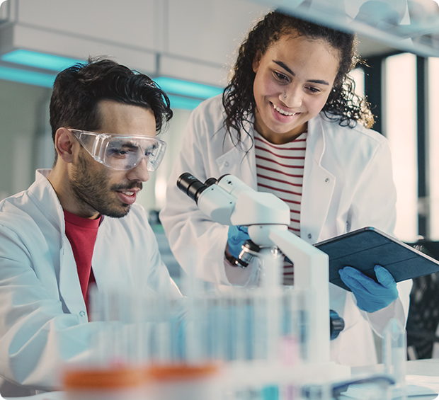 Professionals in a lab look at a microscope.